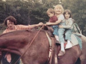 Three small children on a big brown horse being led by an adult woman